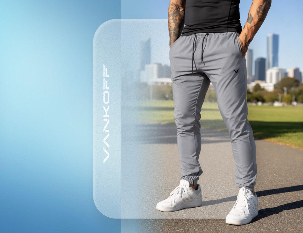 Modelo de calça de tactel cinza Vankoff, em pé num parque, com a cidade ao fundo e céu azul.